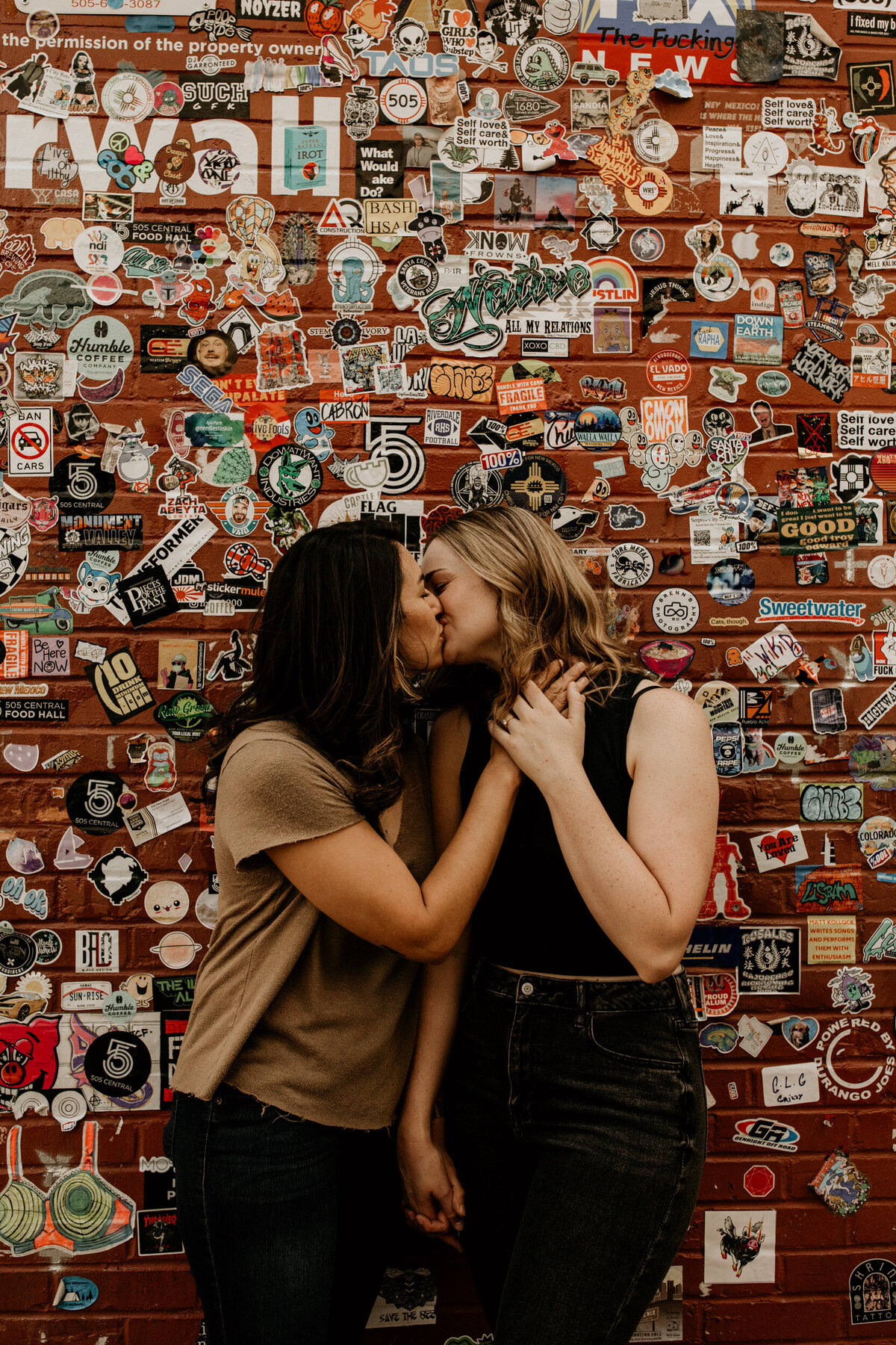 same sex couple kissing in front of a sticker wall in Albuquerque