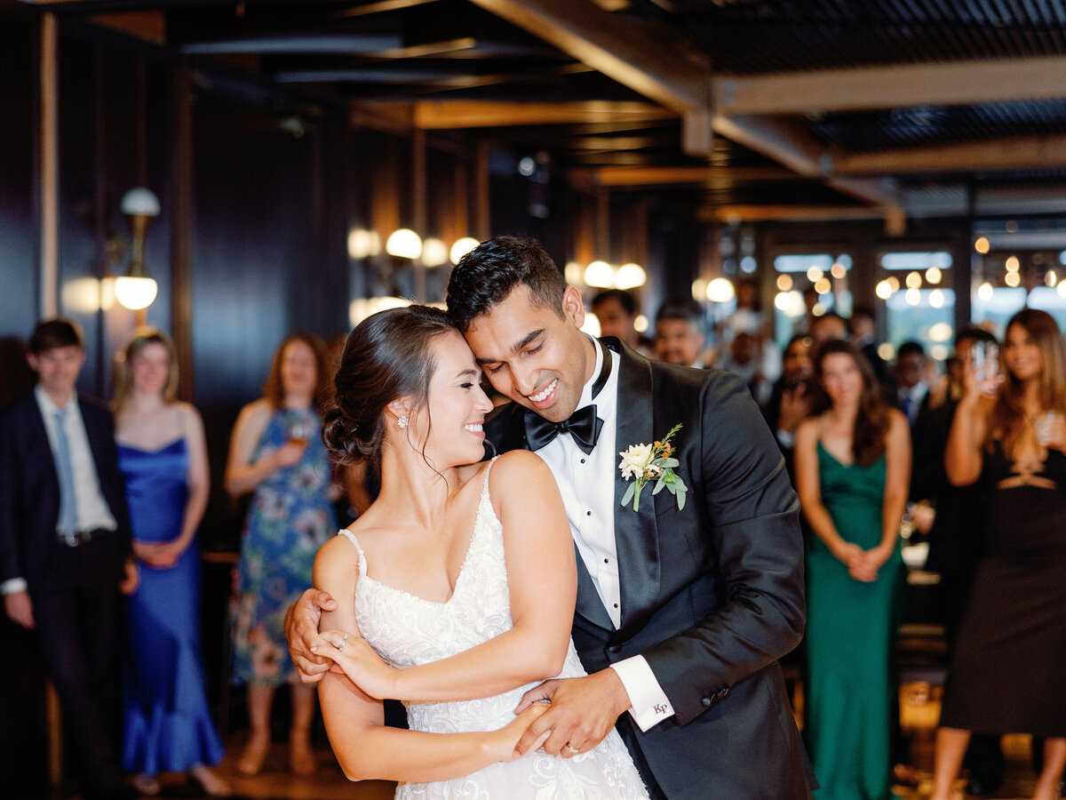 A groom wraps his arms around his bride during their first dance as their friends and family watch