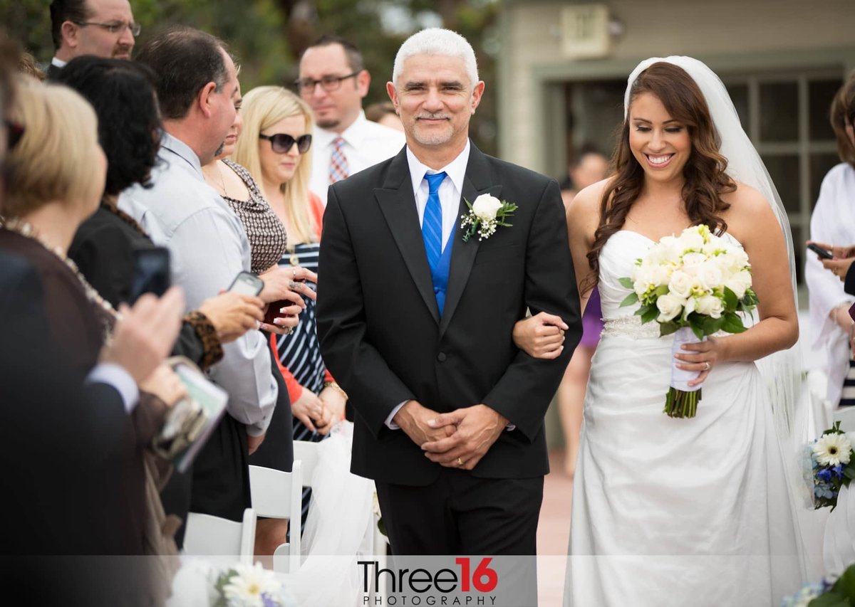 Bride is escorted up the aisle by her father and she is all smiles