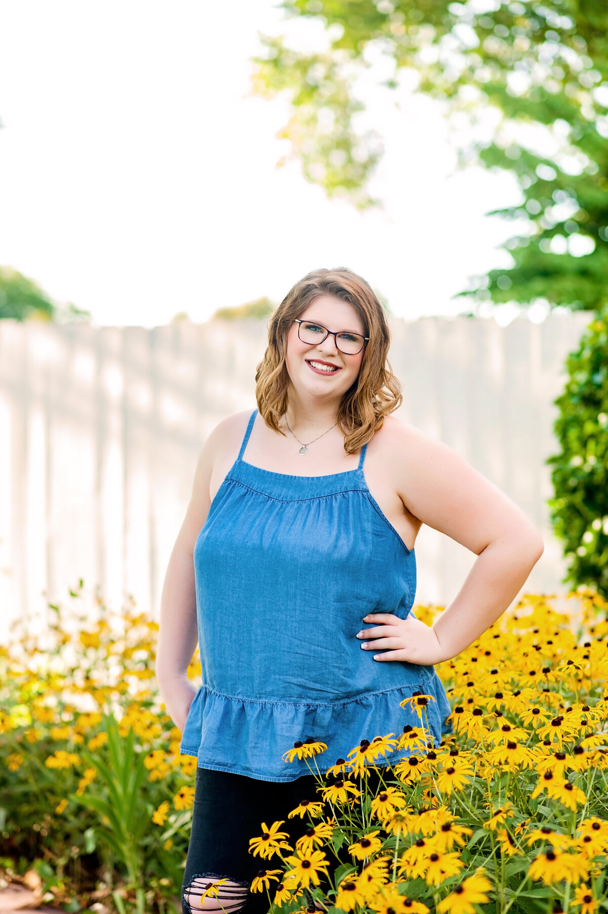 Mechanicsville high school senior girl wearing denim top poses with yellow flowers at Amber Grove venue for her senior pictures.