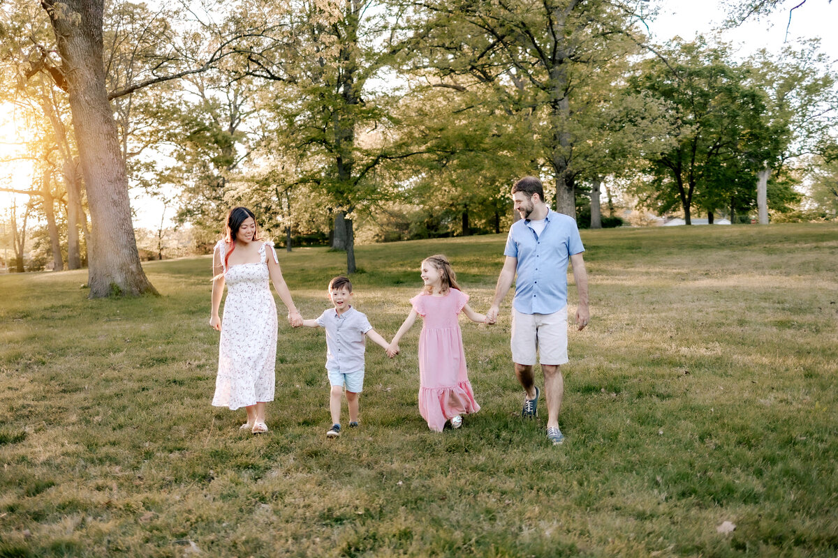 A beautiful young family of four is walking hand in hand through the open field at Sylvan Springs park.