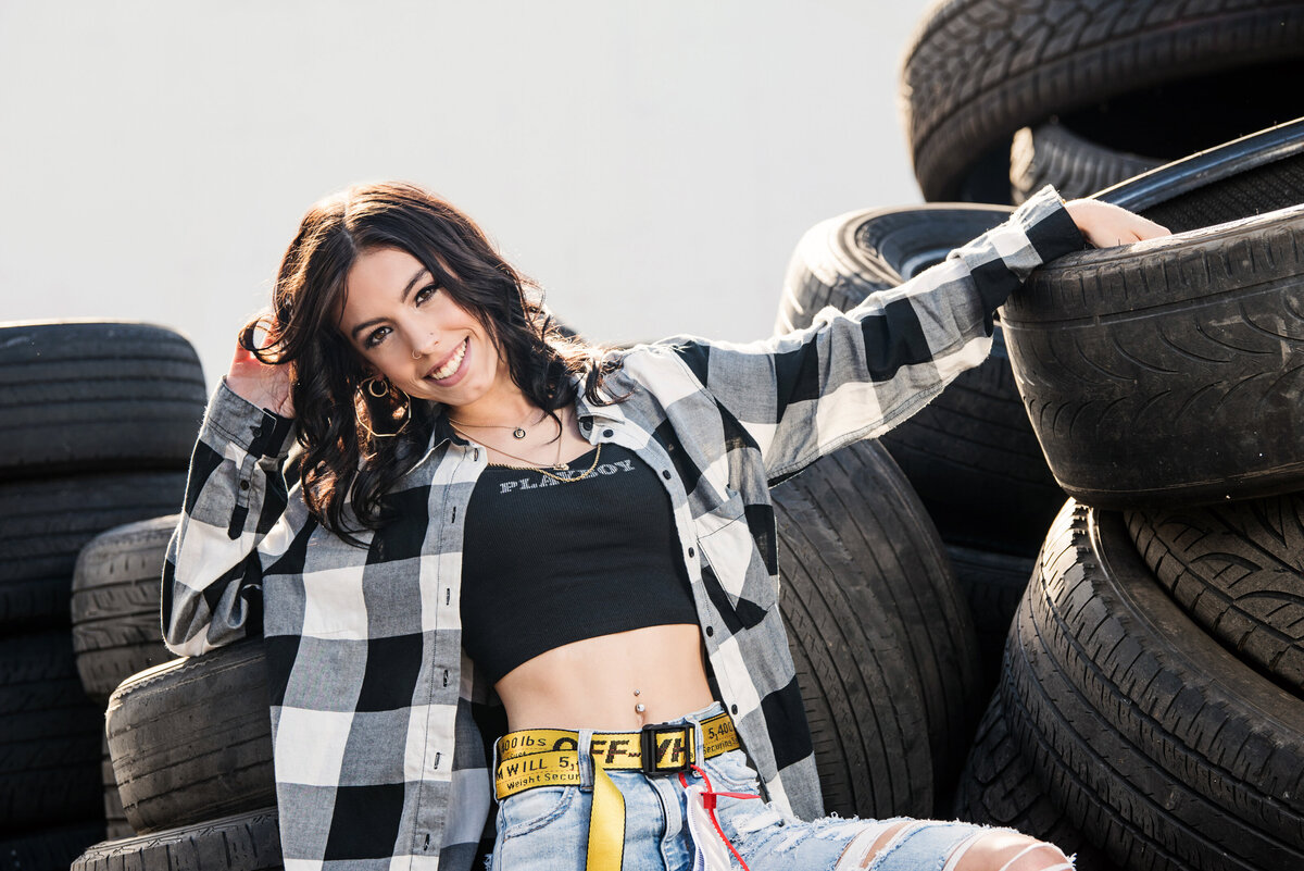 Maple Grove Minnesota high school senior photo of girl with plaid shirt and jeans in a pile of tires