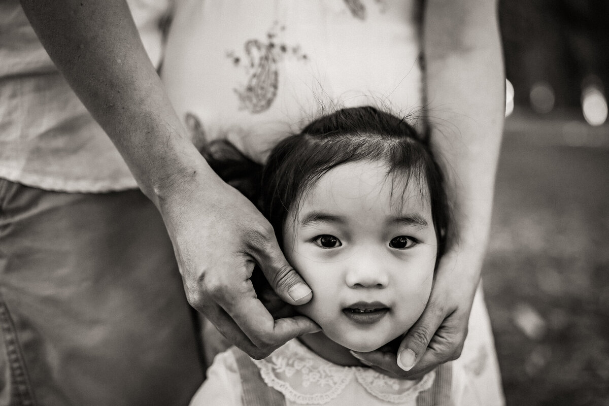 Black and white portrait of young girl with parents hands cupping her face