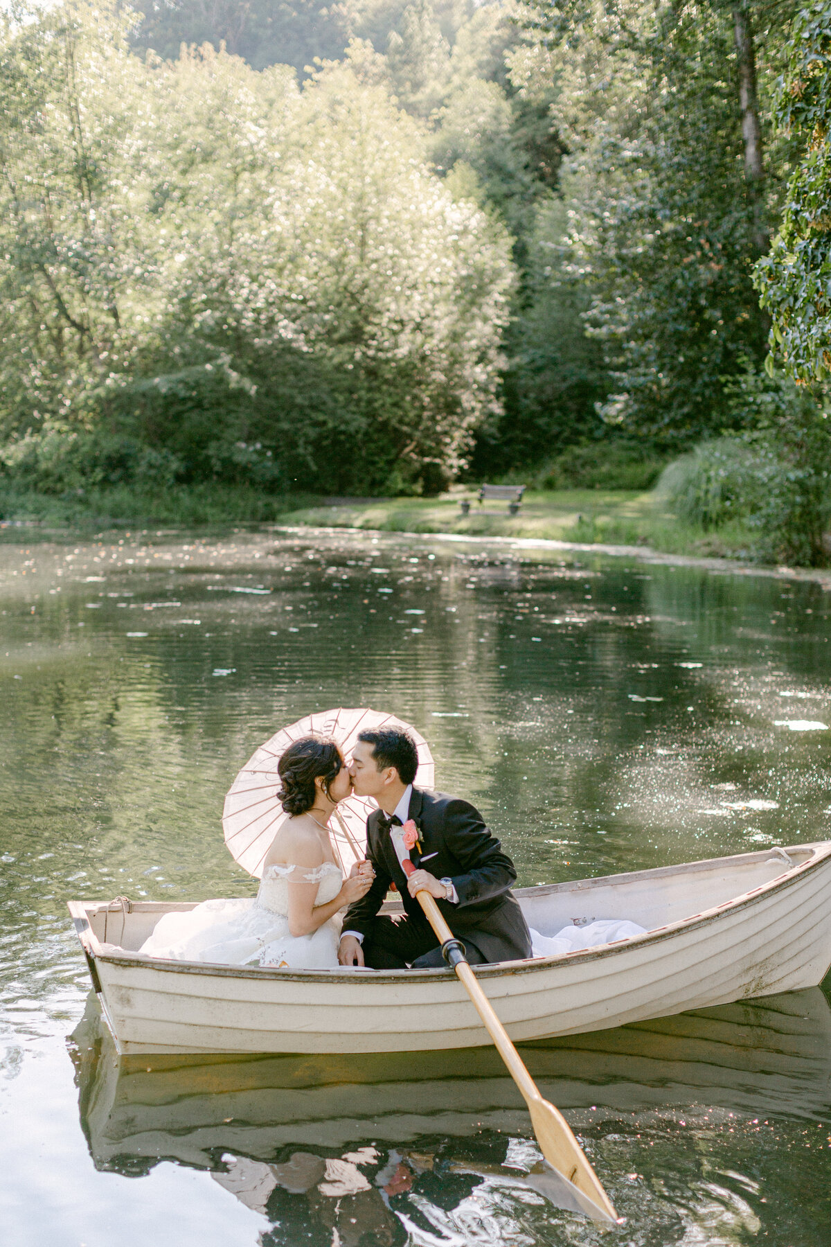 a bride and groom in a canoe with an umbrella kissing with the sun behind them