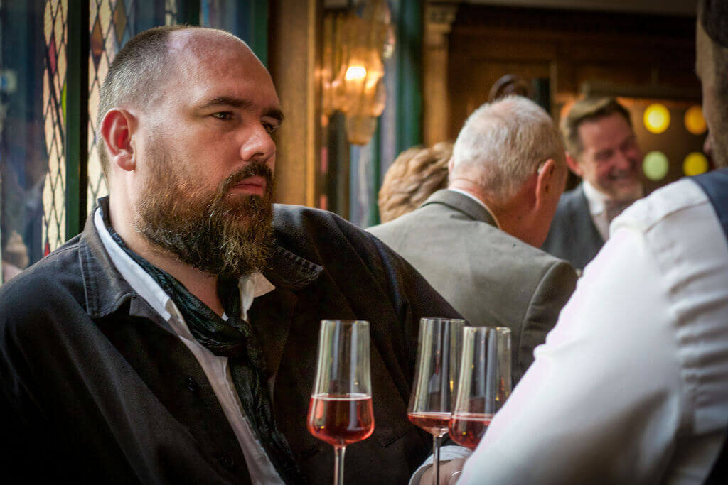 Man looks at another guest listening whilst holding red wine
