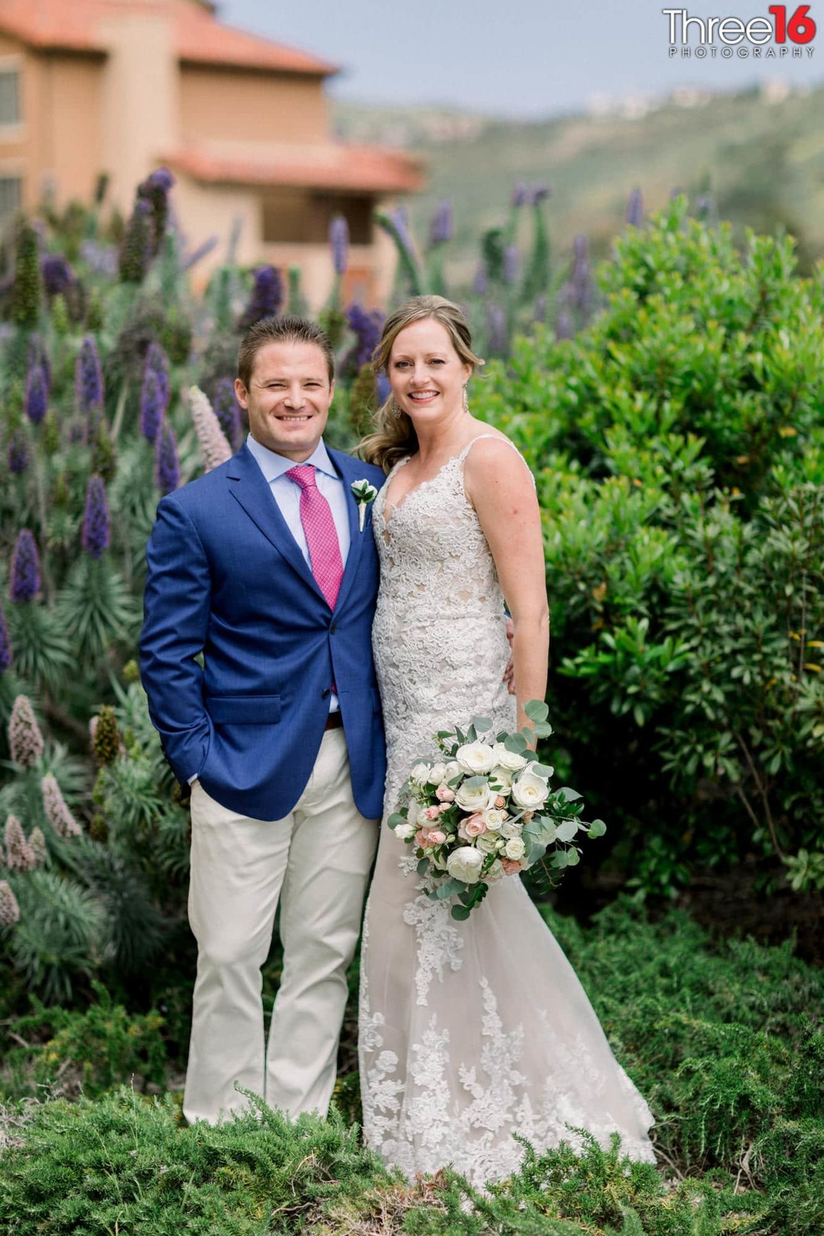 Bride and Groom pose with beautiful green shrubbery behind them