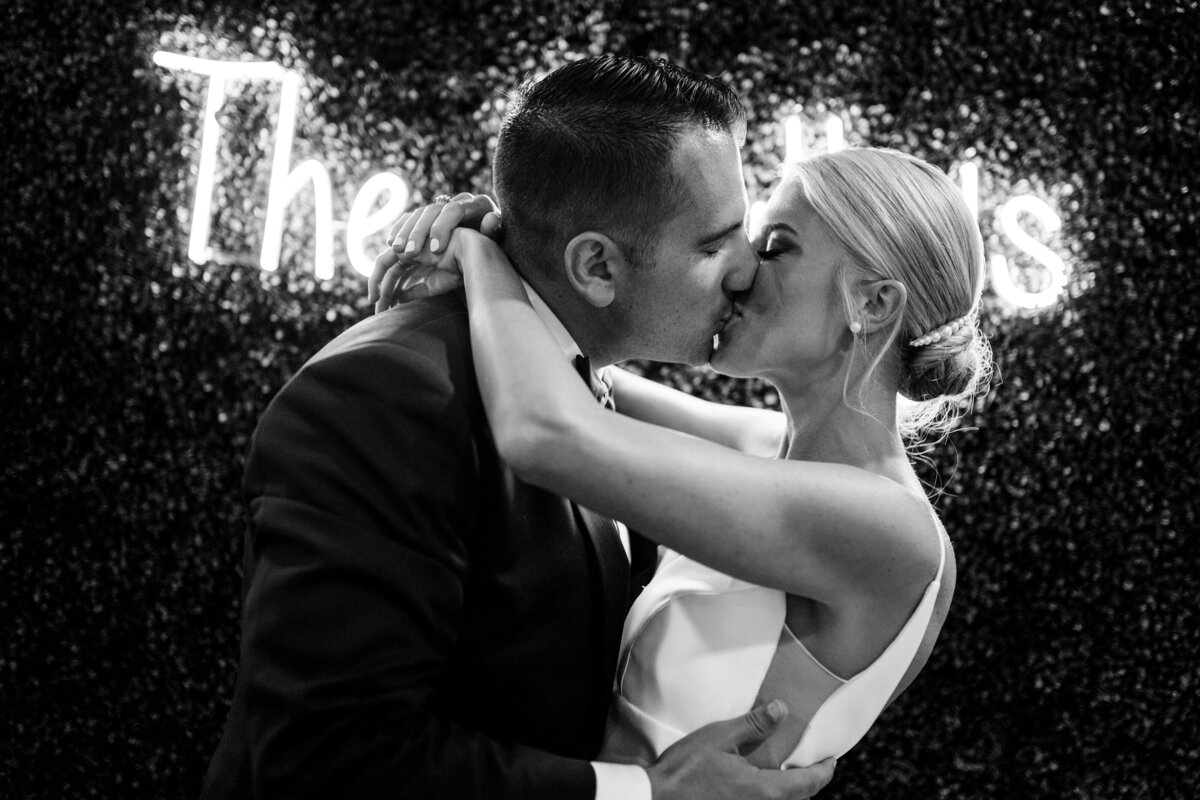 bride and groom kiss in front of neon sign