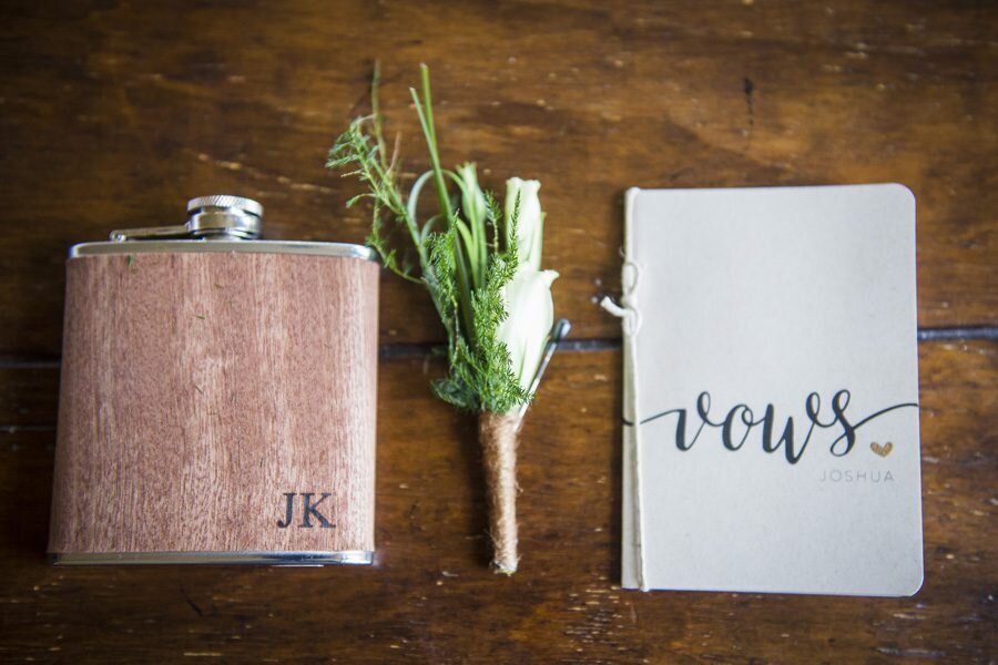 A flask with the initials "JK", a boutonnière, and a small white book that says "vows."