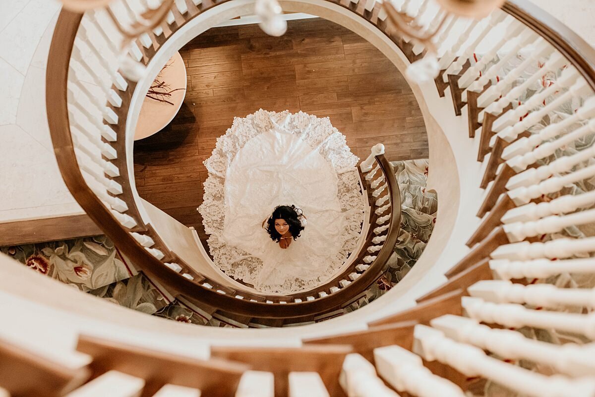 A bride wearing a white lace wedding dress sits at the base of a white spiral staircase at The Estate at Cherokee Dock.