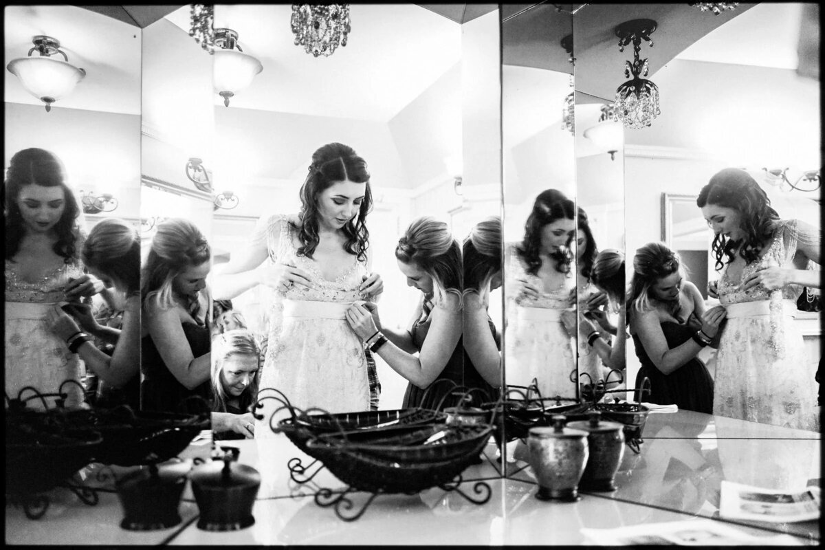 A bride getting ready with her bridesmaids reflected in a mirror, preparing for the wedding in a candid