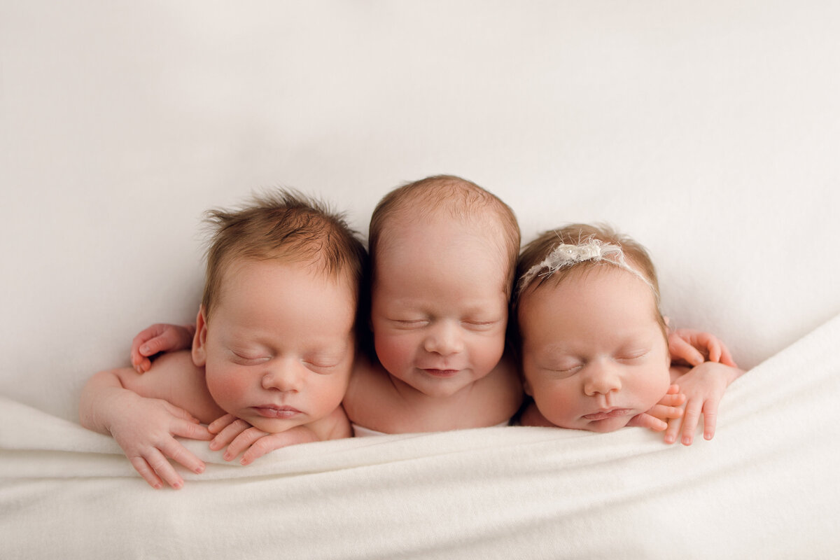 triplet newborn babies on white blanket sleeping