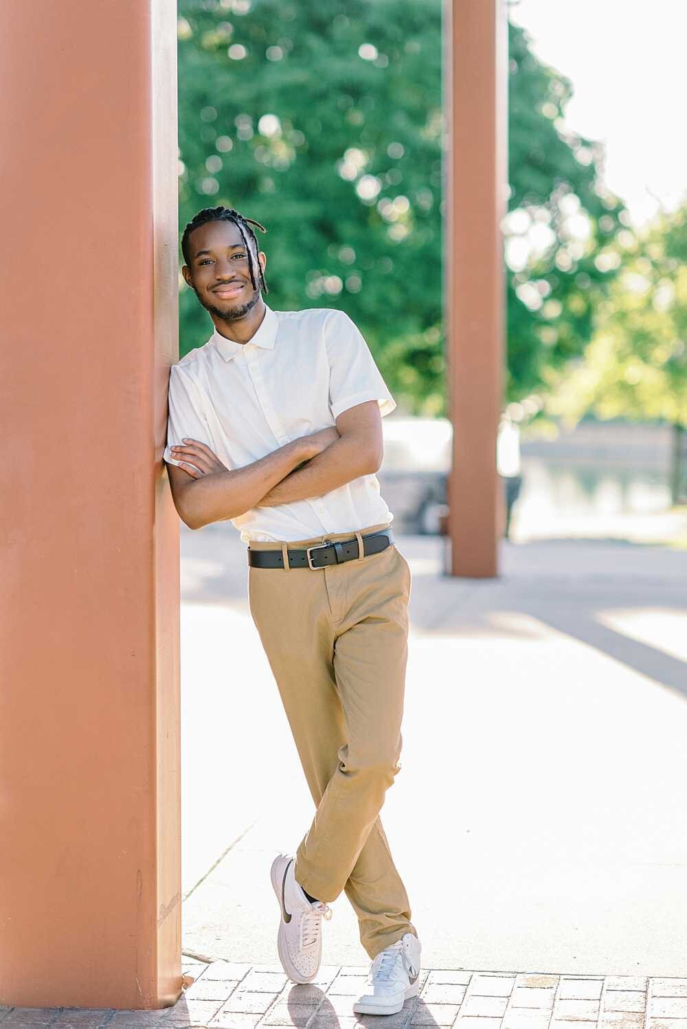 Teen boy with locs, white shirt, and khaki pants leaning on a pillar
