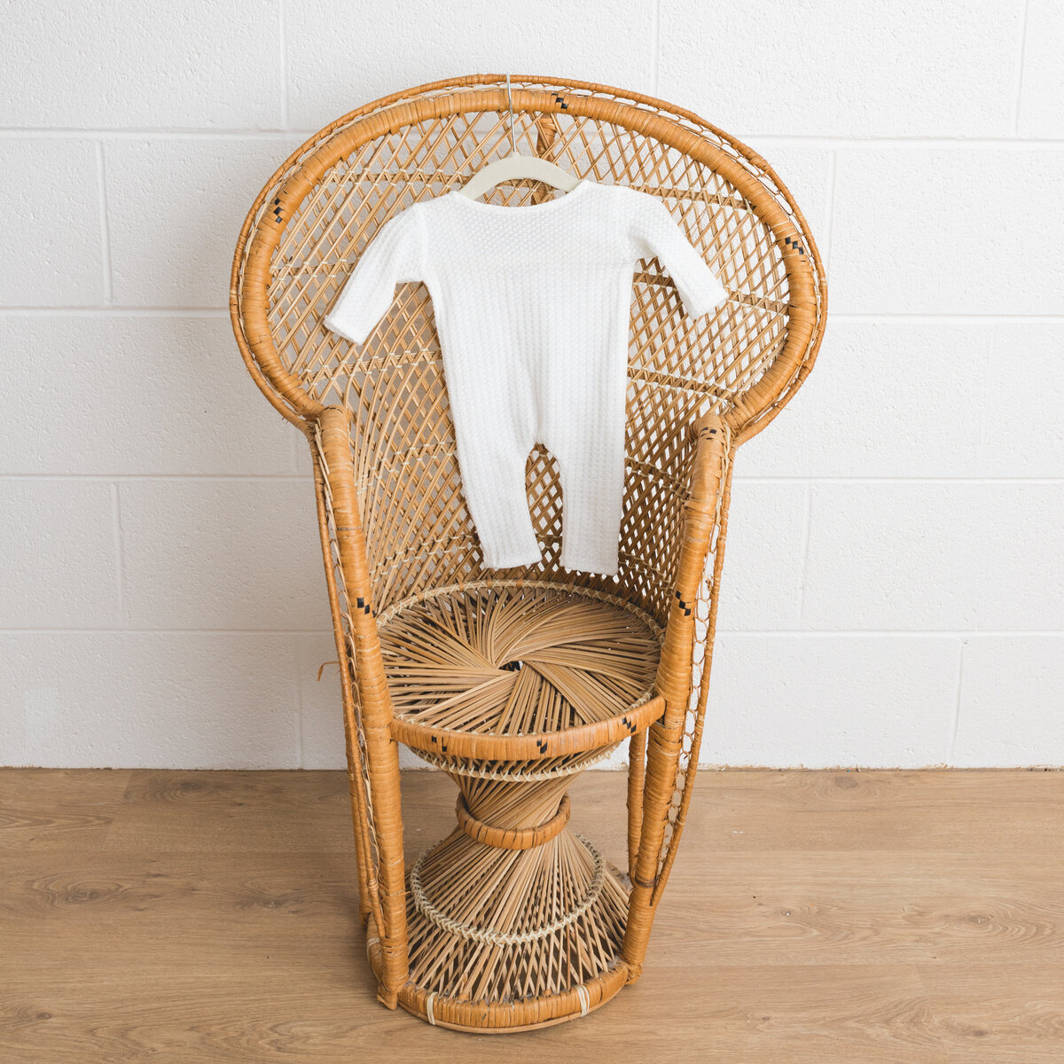 Image depicts a miniature peacock chair in a photography studio on the chair hangs a tiny newborn outfit in white knit  with  a waffle weave.  This image is a sample of Lauren Vanier Photography's newborn client wardrobe. Image taken in Hobart Tasmania