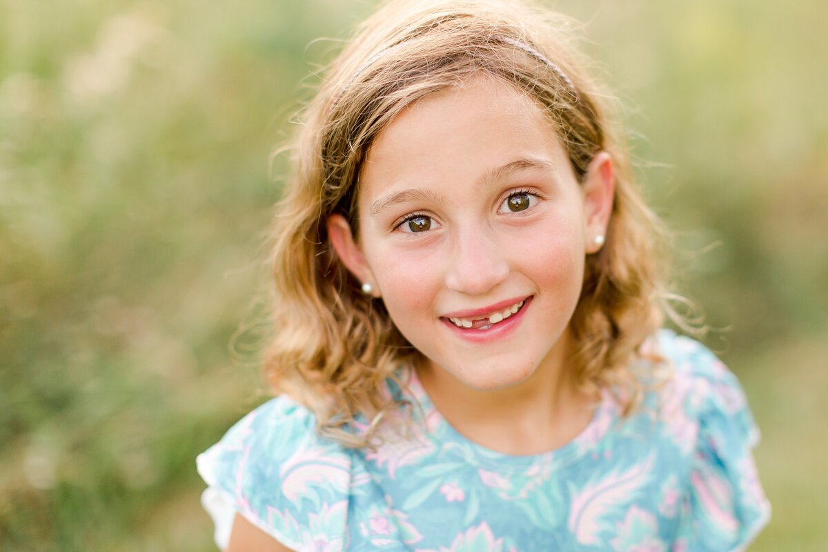 A little girl smiling big in a field at a family photo session in Lexington KY.