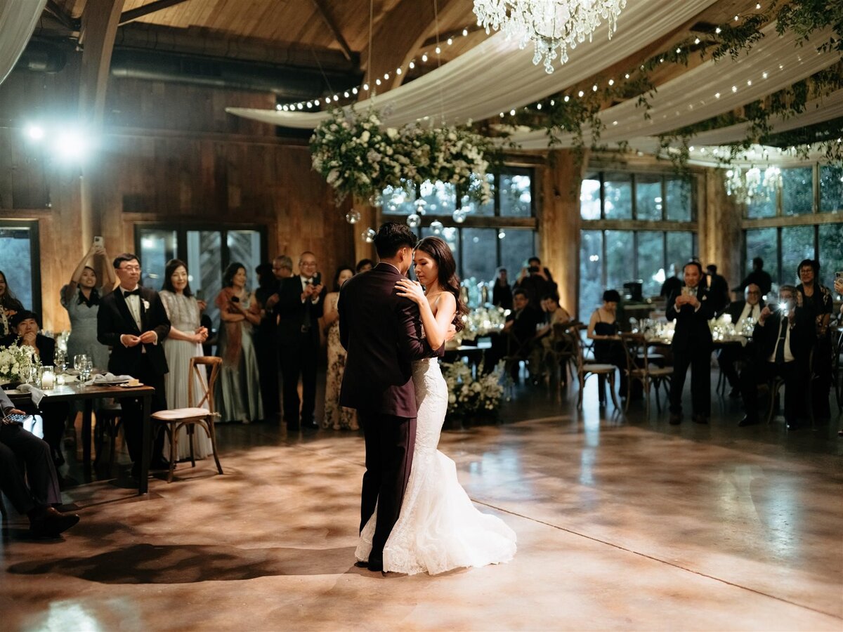 Bride and groom's first dance on wood dance floor under chandelier, twinkle lights, and white swagged fabric at Cedar Lakes Estate