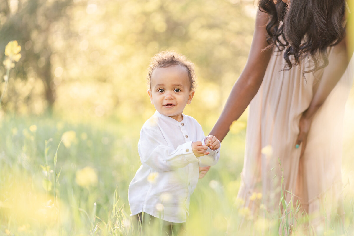 Little boy in a white shirt holding his mom's hand in a field of mustard flower in the san francisco bay area