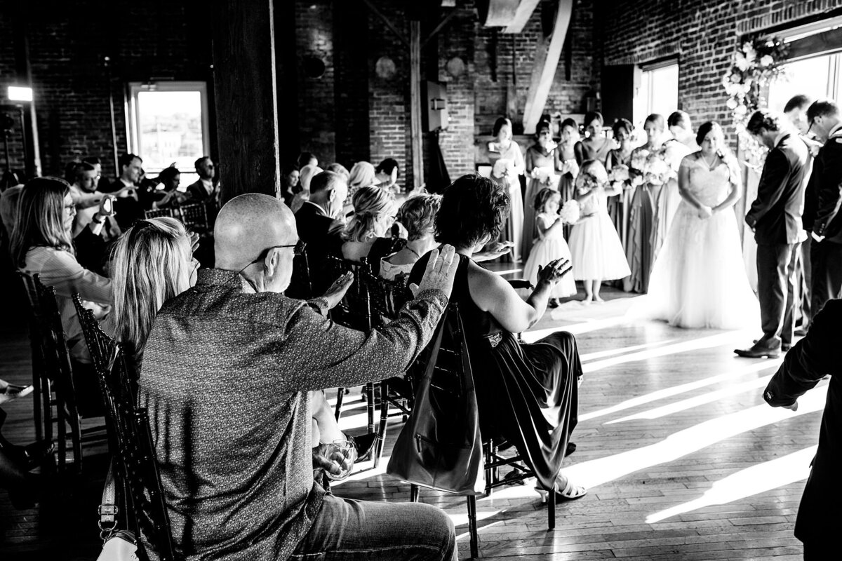 Black and White photo of guests praying over couple during their vows