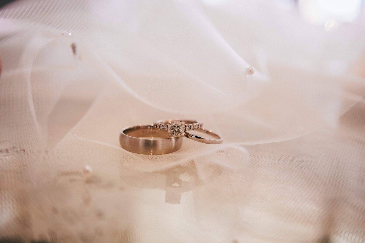 Gold wedding bands lay on a bed of lace and pearls.