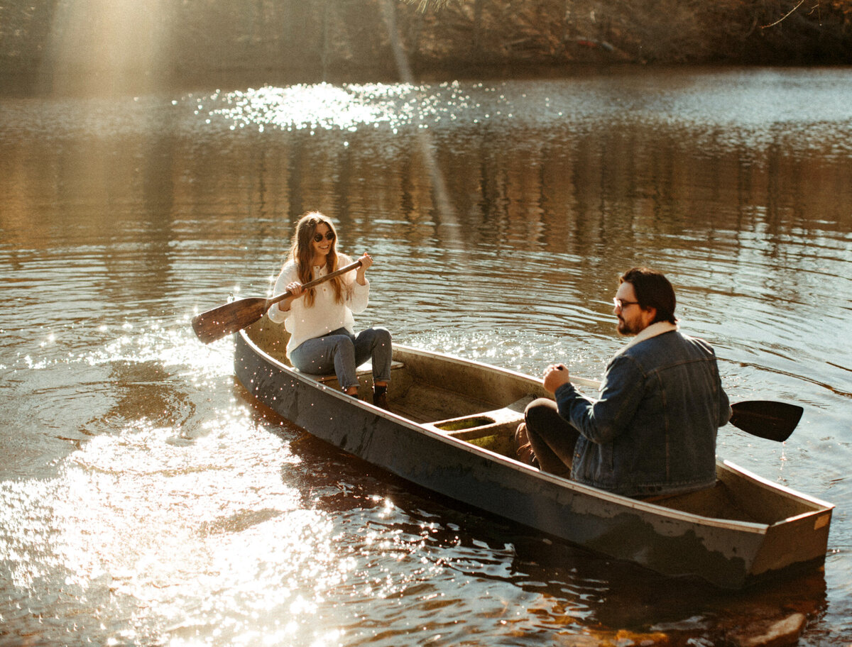Couple in a boat rowing out onto a lake as the sun glistens on the water around them