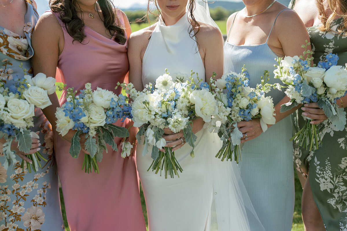 Close-up of a bridal party wearing mismatched floral dresses and holding lush bouquets of white and blue for a summer wedding in Jackson, WY.