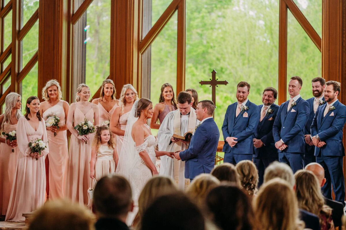 photo of a wedding ceremony in a glass chapel as the groom puts a ring on the bride's finger