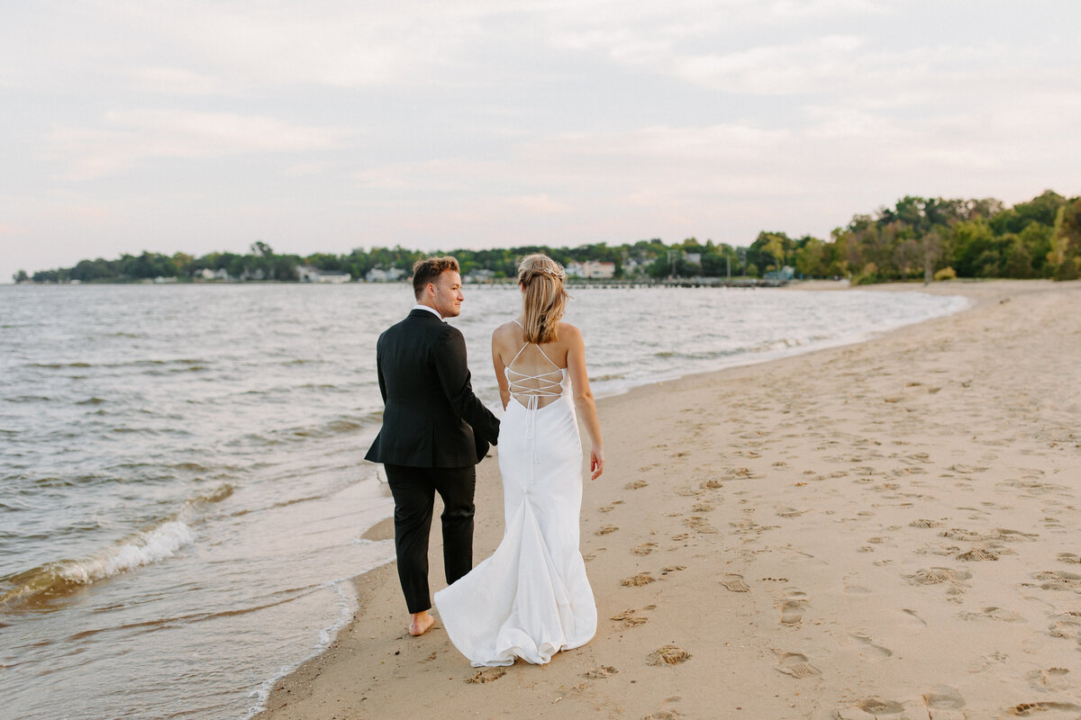 bride and groom holding hands walking down the beach looking at each other