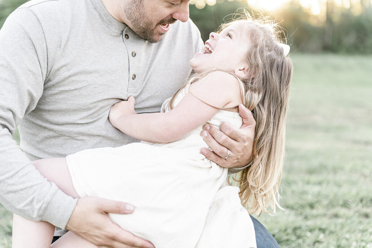 A father hugs his daughter in a field at sunset by Nashville family photographer
