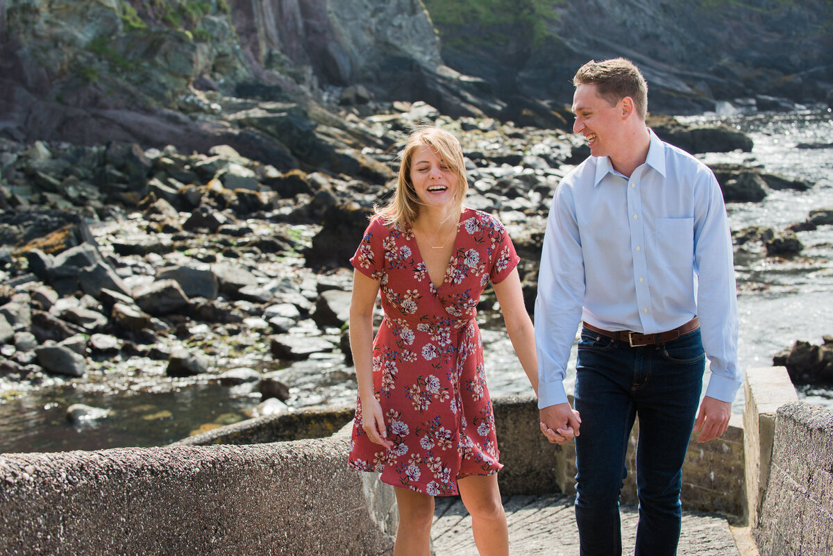 young couple walking up pier, holding hands and laughing in the sunshine