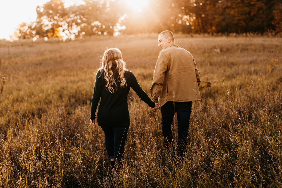 couple holding hands walking in a field at sunset