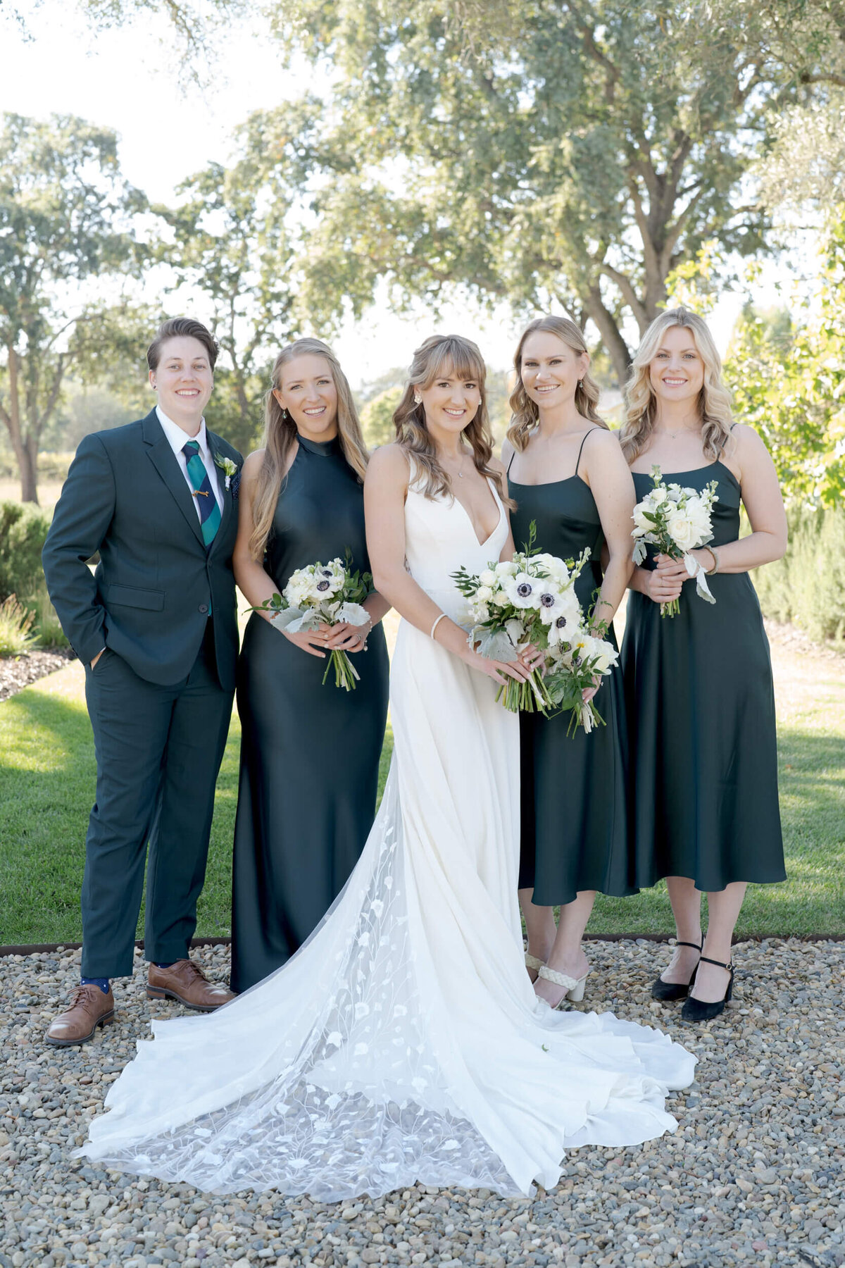 Lovely bride in white gown poses with her family and bridesmaids dressed elegantly in black.