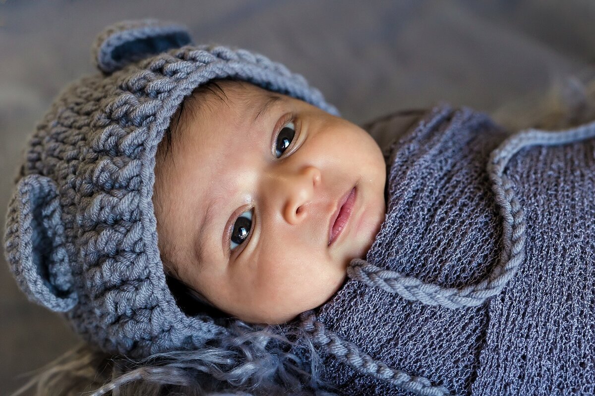 At home newborn session of Indian baby born dressed in blue wrap and blue hat looking at the camera