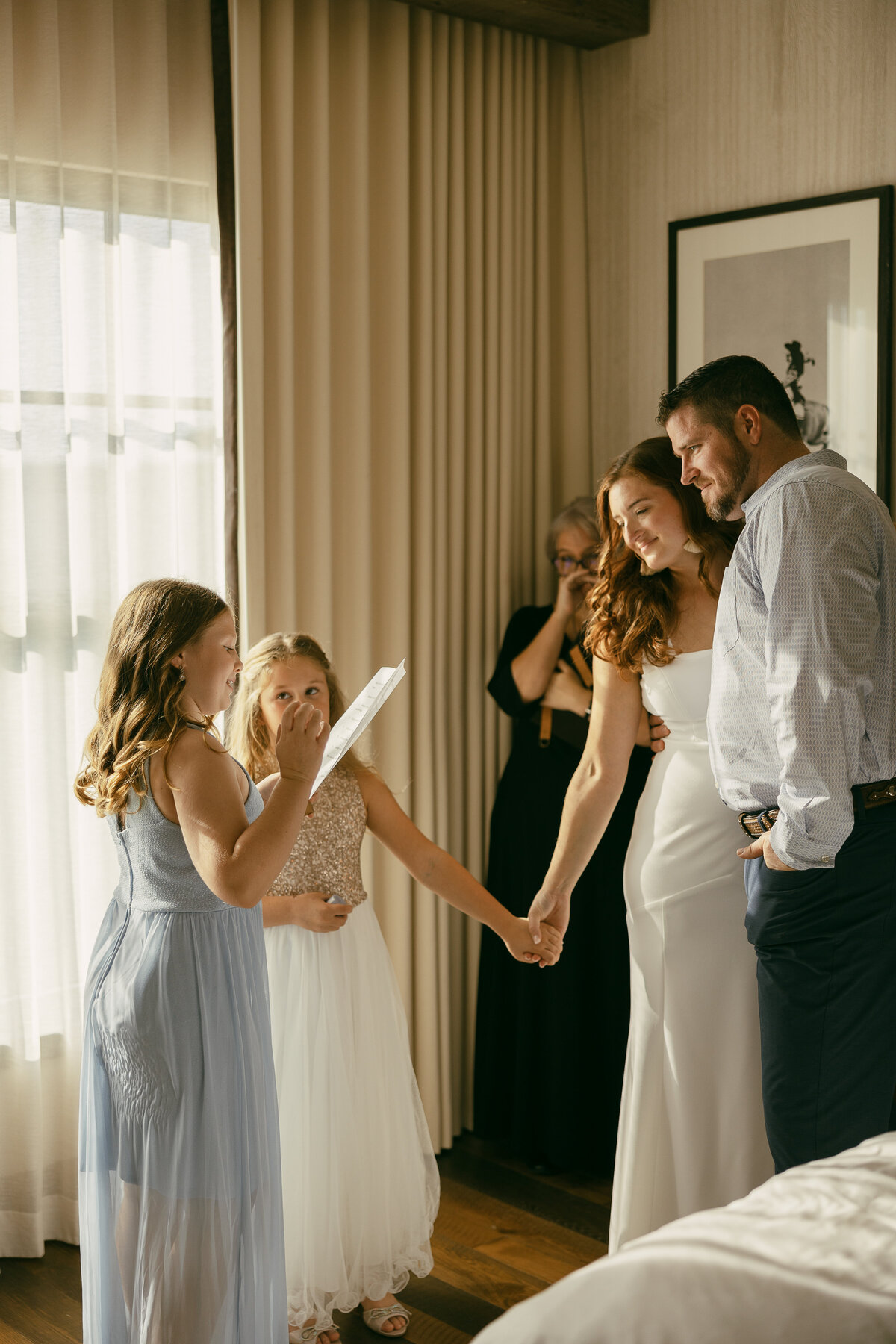 A wedding couple standing together as two kids read a letter to them.