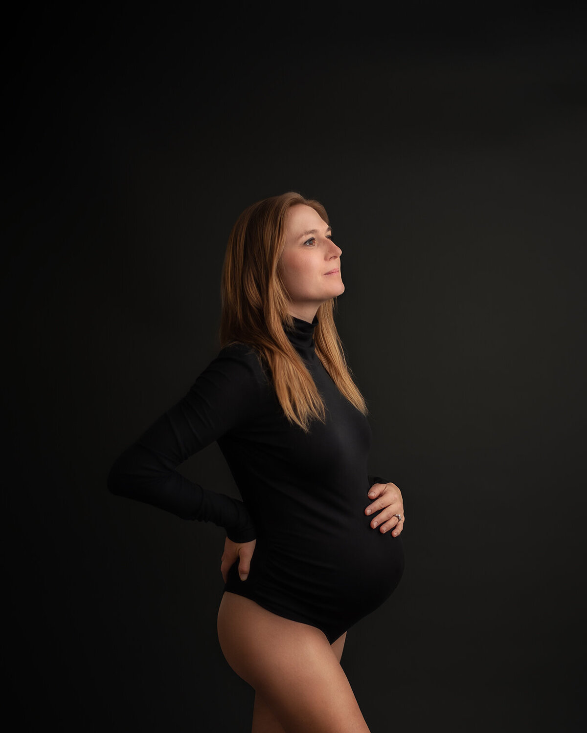 pregnant woman in black bodysuit on black backrgound at maternity session