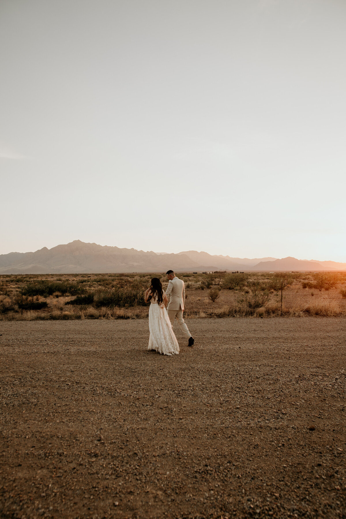 bride and groom walking in the desert together at sunset