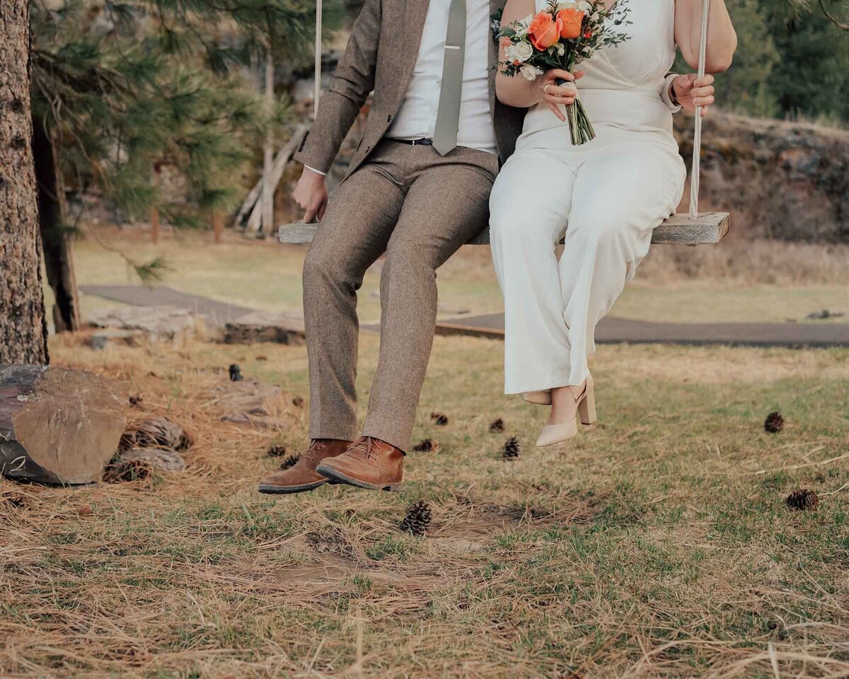 Maddie Rae Photography bride and groom sitting on a swing. their feet are hanging. she is holding her flowers. no faces are seen in this image