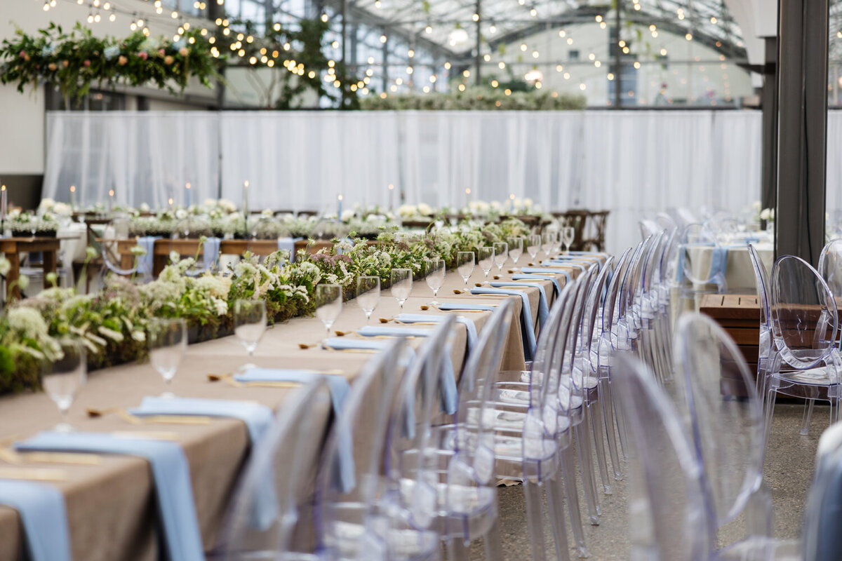 Acrylic chairs, caramel table clothes and greenery at the wedding reception.