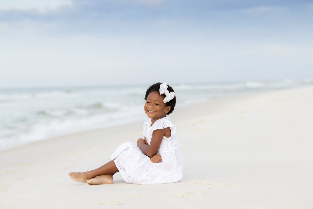 A small girl smiling and sitting at the beach