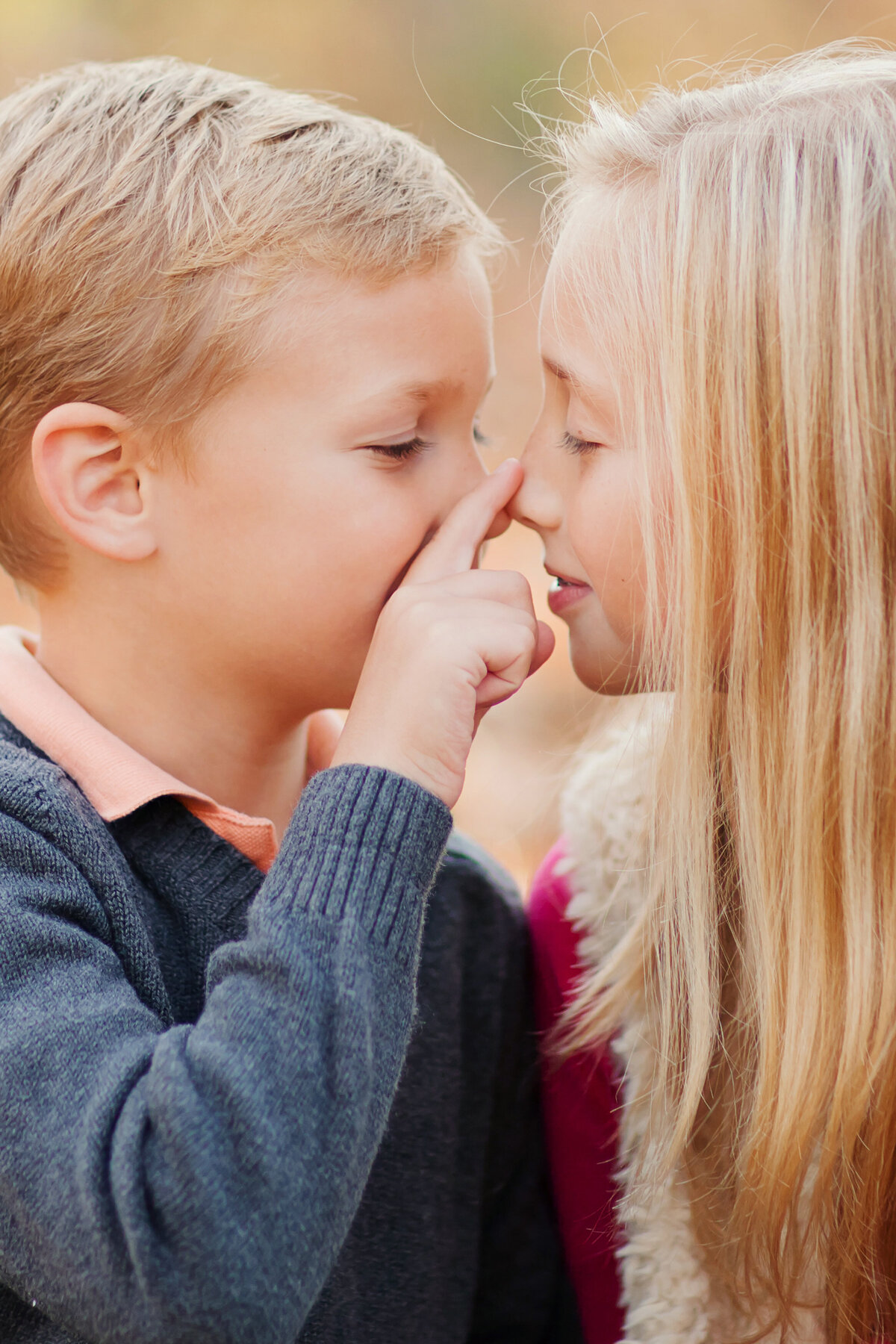 Siblings are nose-to-nose, and he is gently touching her nose with his finger in this sweet photo.