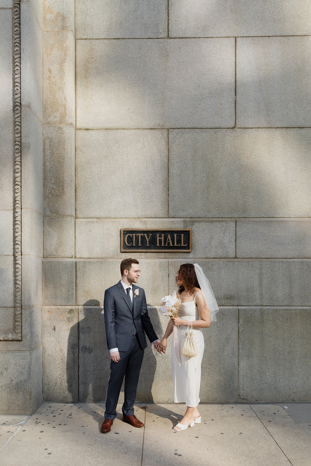 Just Married photo session couple holds hands and looks at each other under Chicago City Hall sign