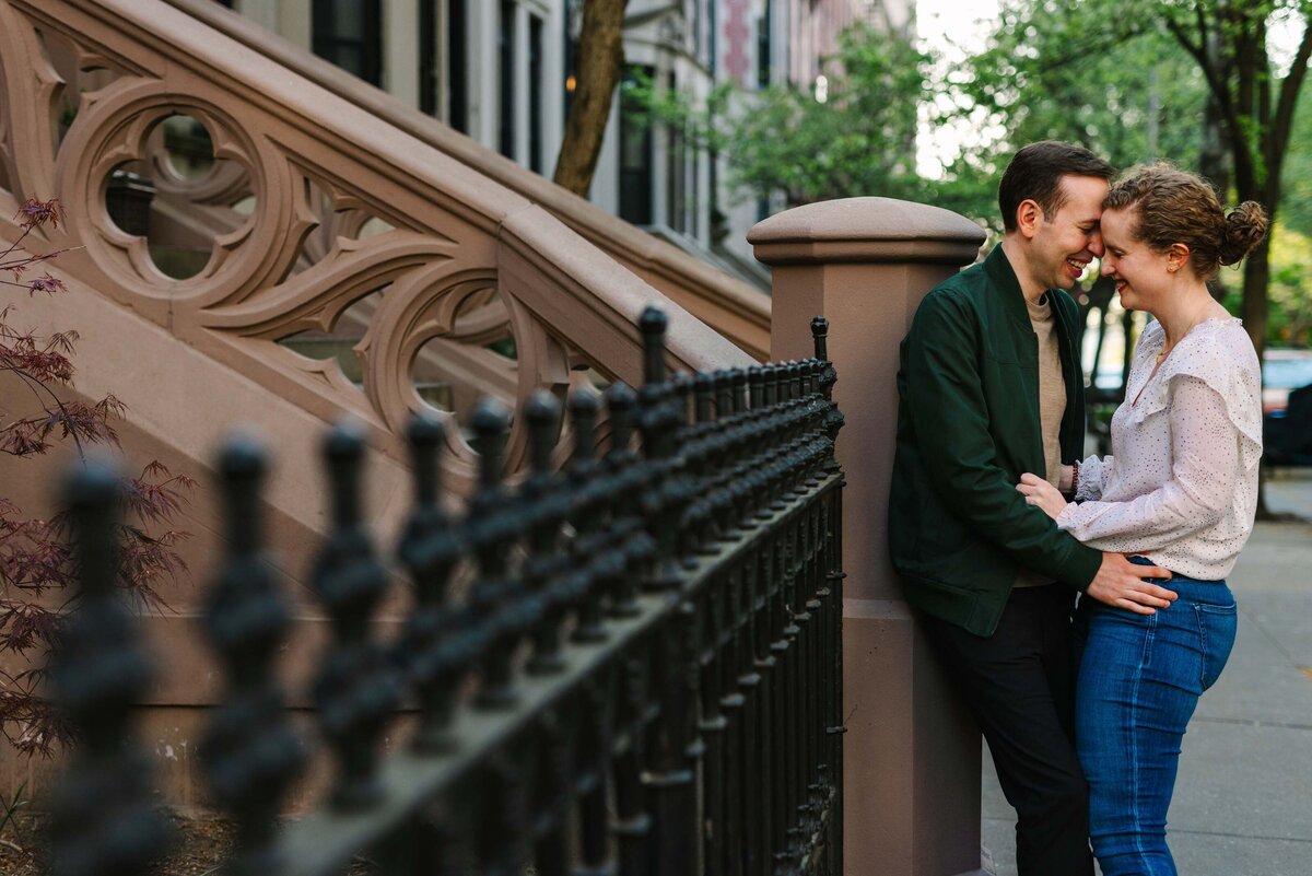 A couple leaning up against the staircase to a brownstone about to kiss.
