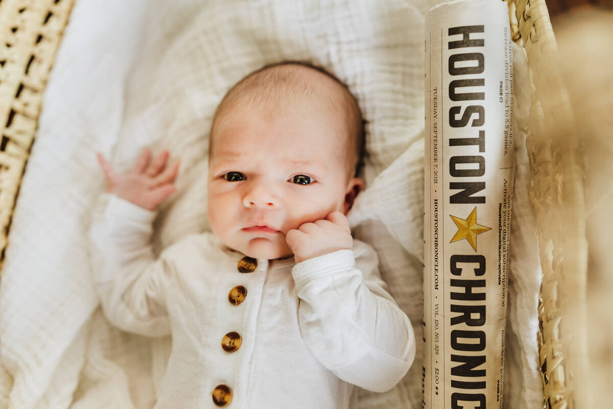 Newborn son laying in moses basket next to the Houston Chronicle Newspaper, with the headlines from his Birth Date.