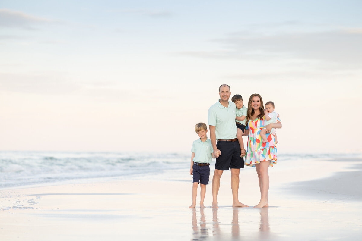 Two parents each holding a baby with another child standing next to them at the beach in Watercolor Florida.