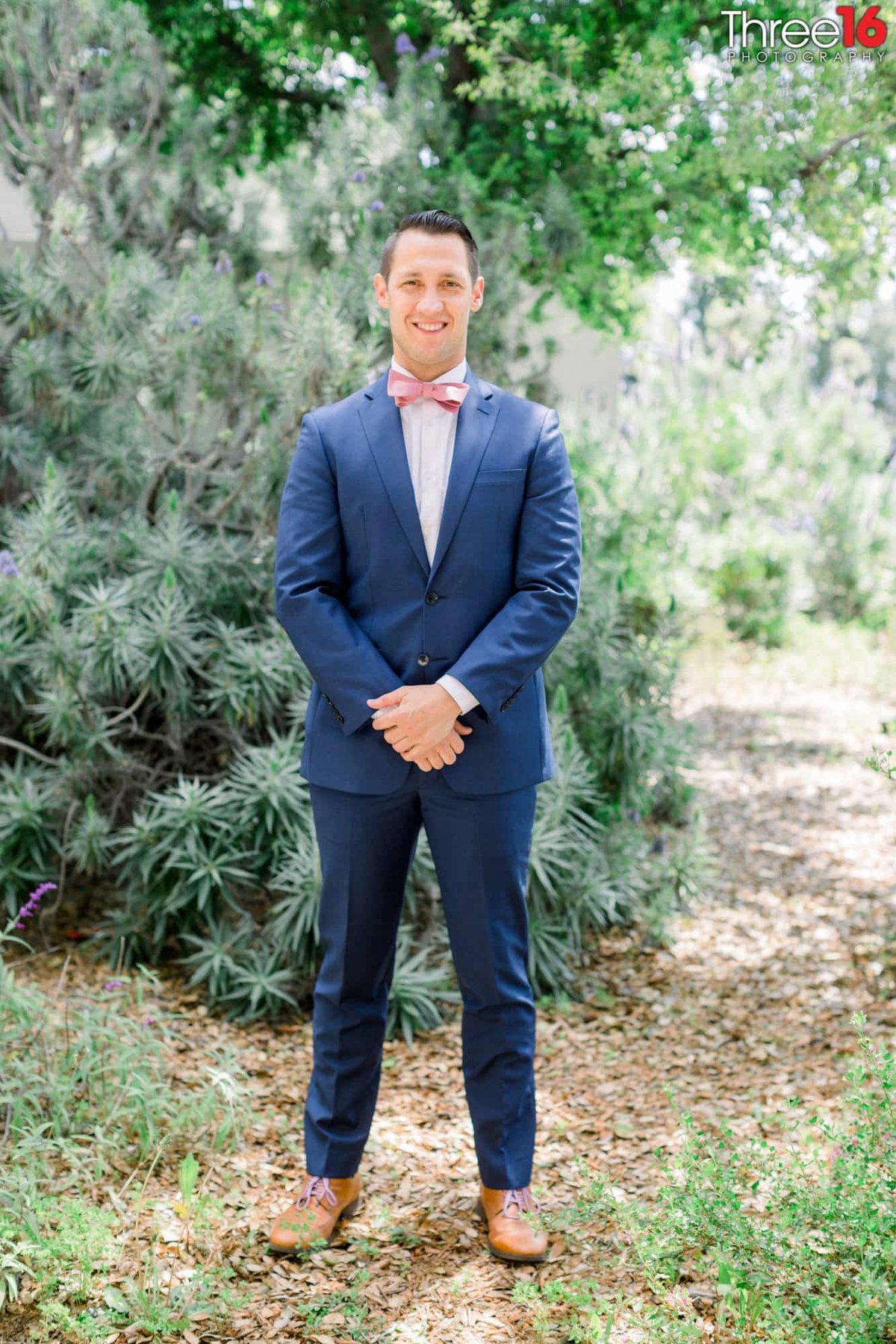 Groom poses in front of green bushes prior to the start of the wedding