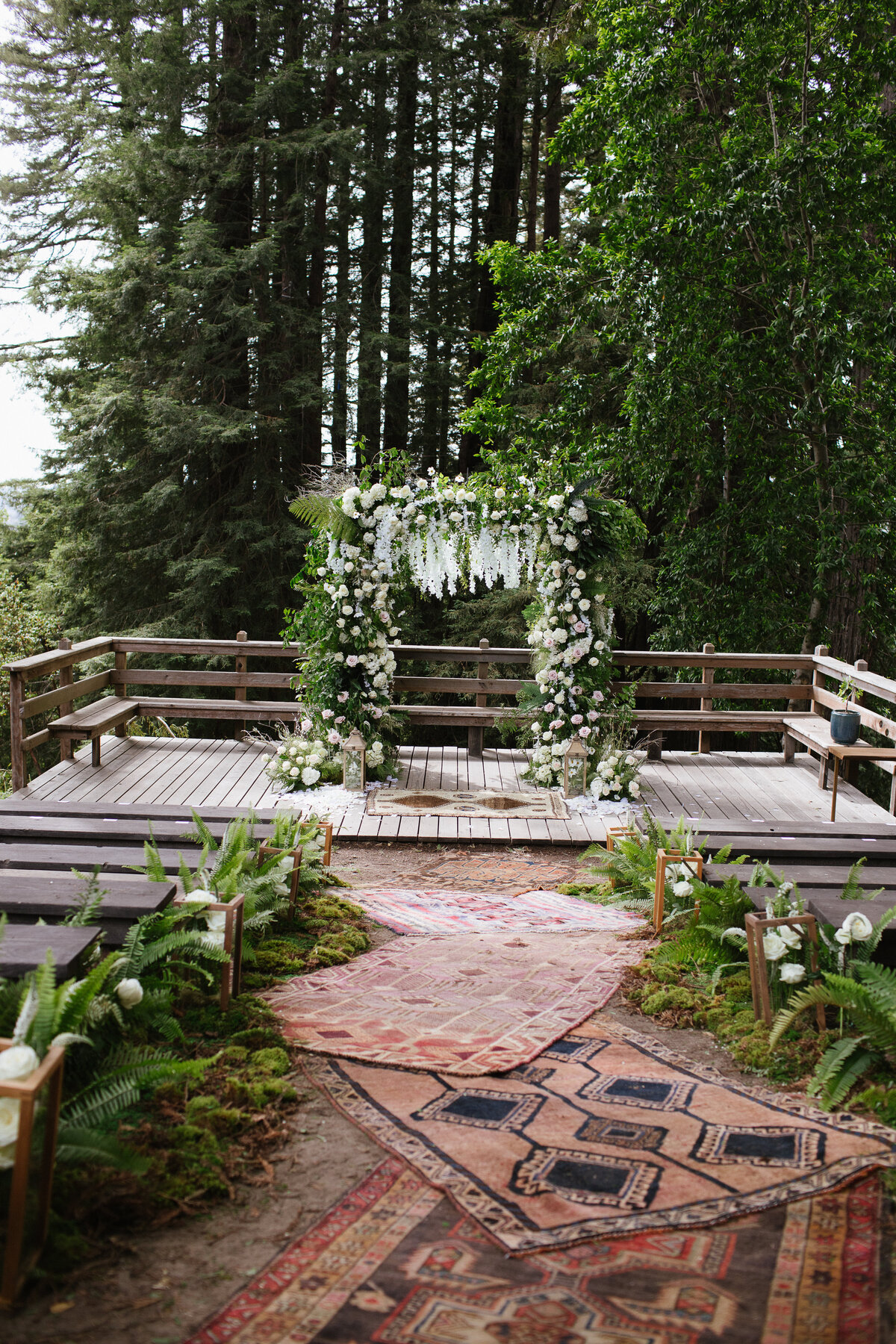 Ceremony with benches, rugs, and hanging flowers on an arch in the redwoods