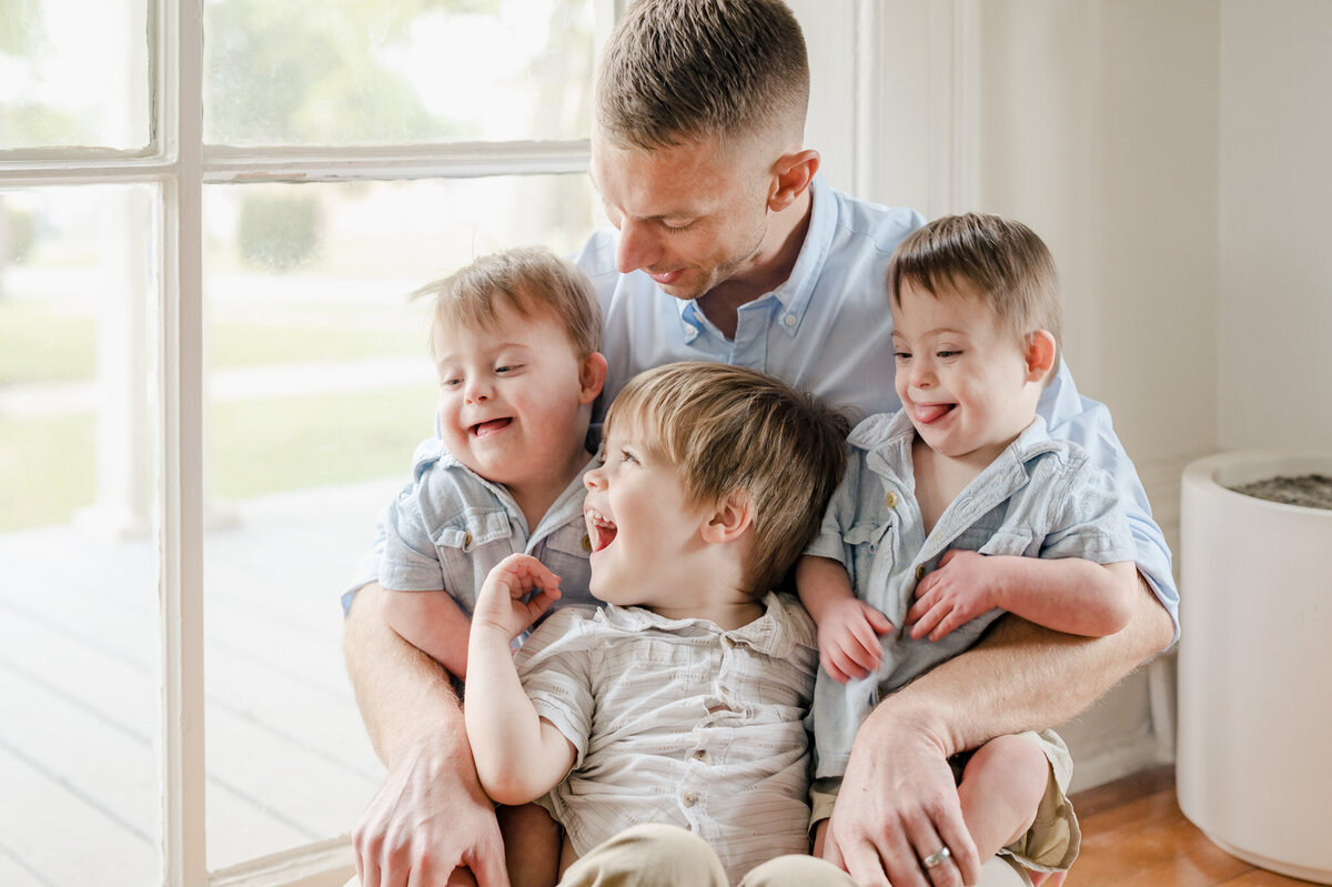 Dad sits inside a window holding three young boys on his lap.