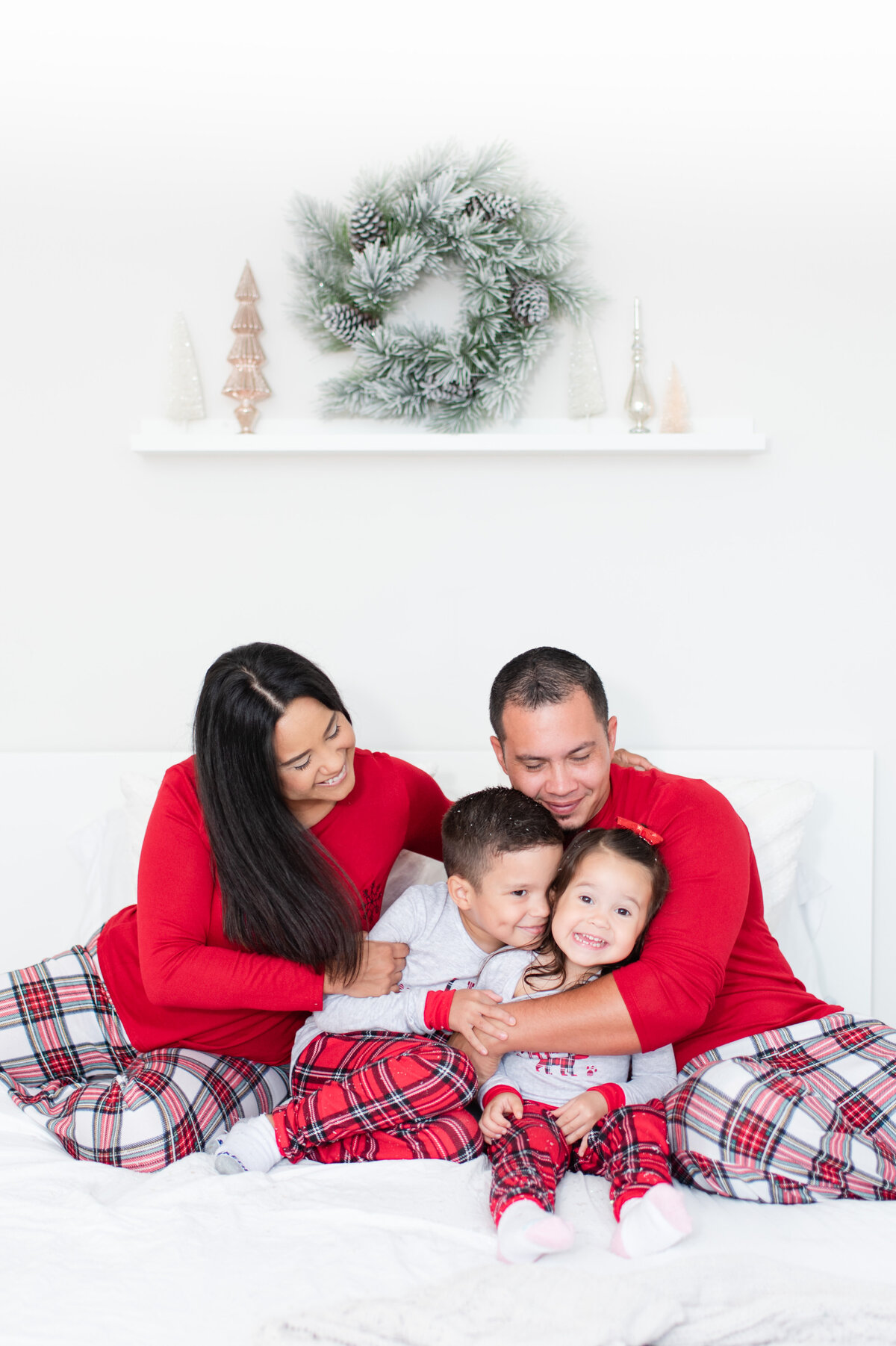 family of four matching Christmas pajamas on the bed with snow at Christmas  by Miami Christmas Mini Session Photographer MSP