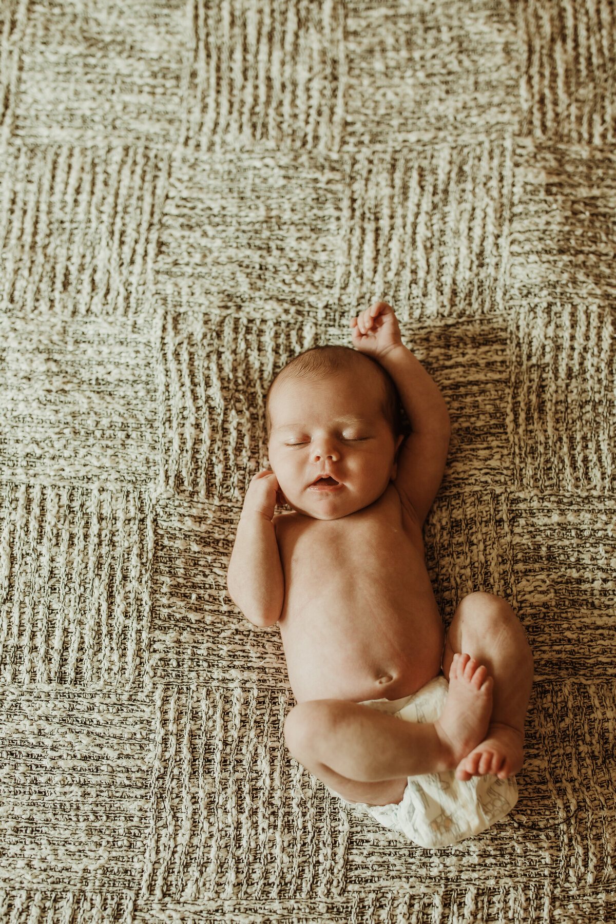 Infant in diaper on textured backdrop stretching one arm