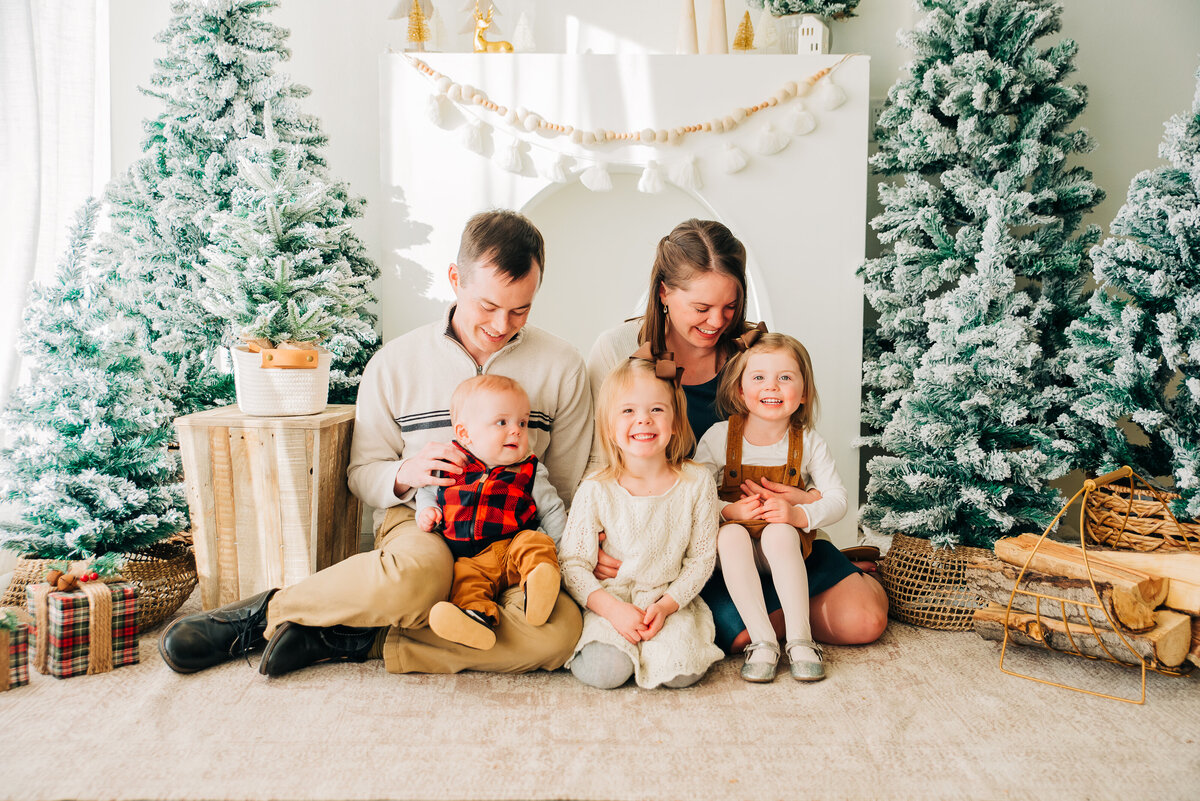 denver family photos with  mother and father sittignw ith their three children in front of a winter wonderland backdrops taken by colorado wedding photographers