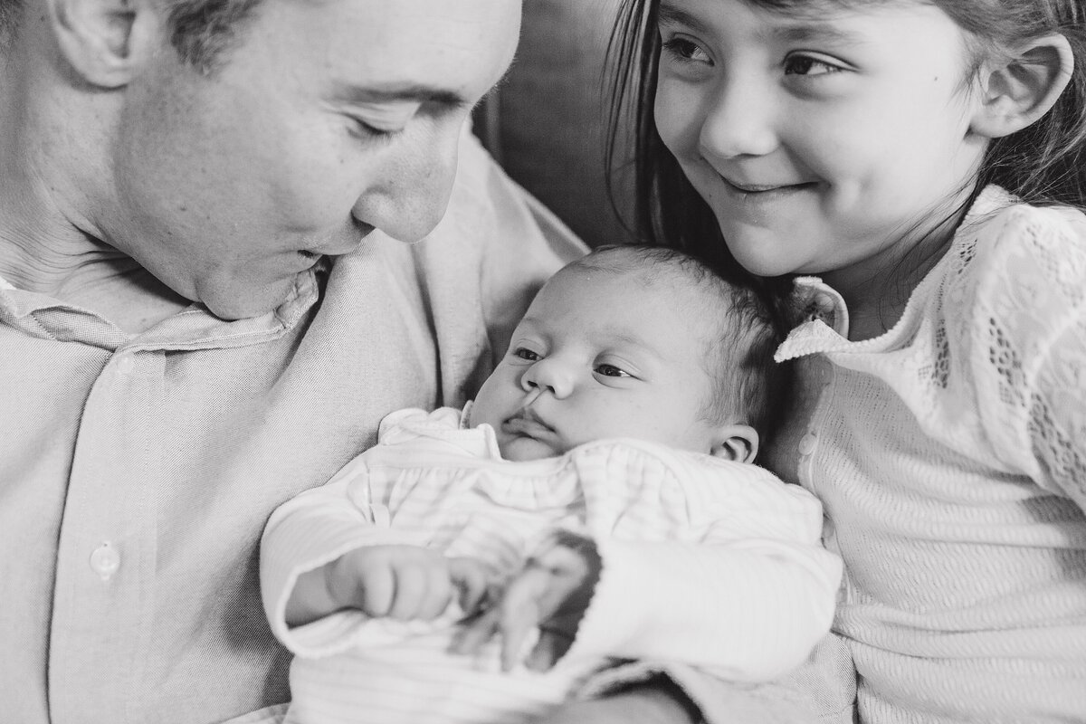 Black and white image of a father snuggling two daughters during an in-home newborn session in KY.