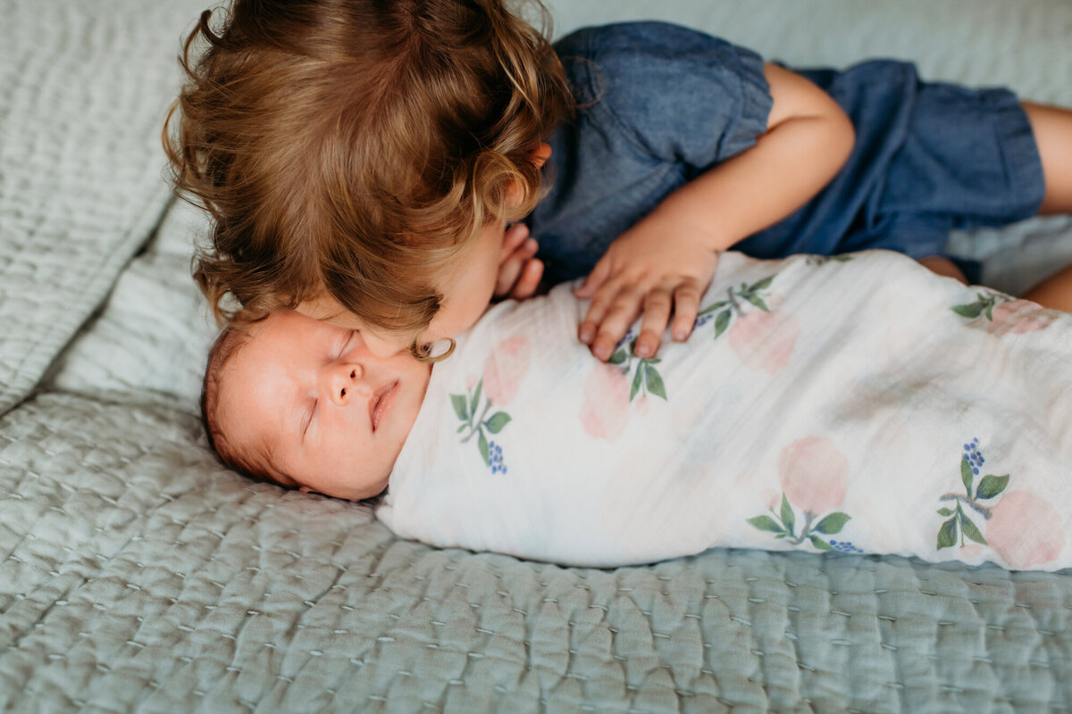 Newborn Photographer, Little boy snuggling and kissing baby girl in a flower blanket.